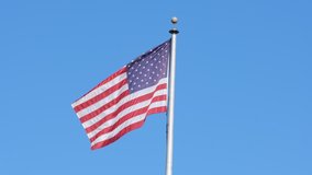 High definition 4k video of American flag flying high on a pole against blue sky background on a clear windy day closeup