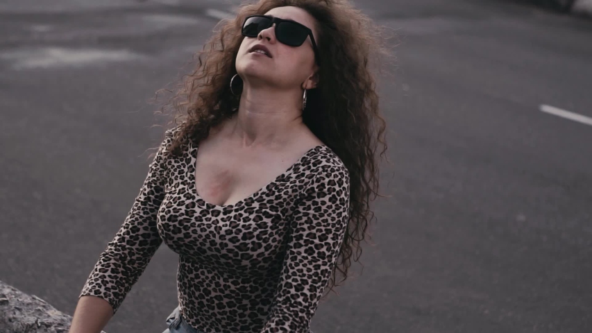 Pretty smiling curly woman in stylish look and suglasses touches hair bright sunlight, have fun, smiling and walking in the city