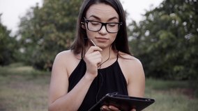 the girl in glasses walks in the Park and looks at the tablet, talking to friends and family.