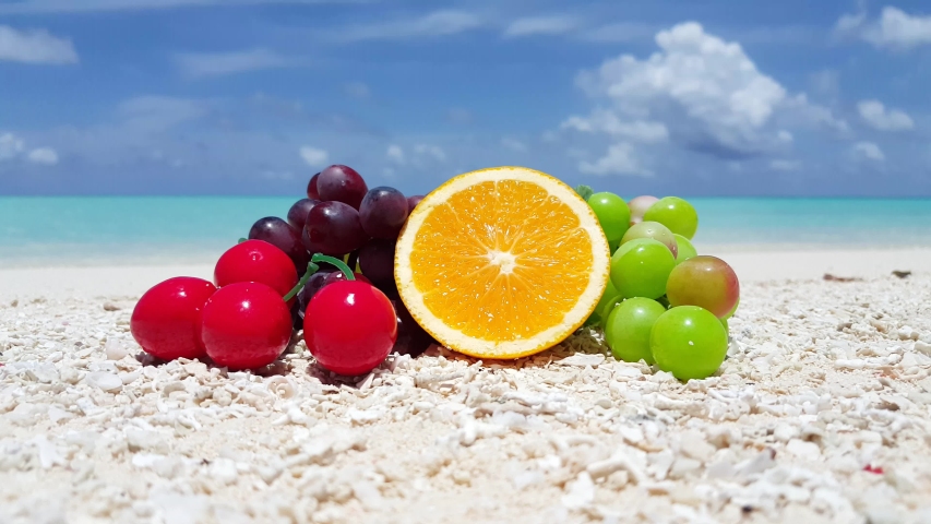 Assorted fruits on the beautiful white sand beach of Hawaii under clear blue cloudy skies - Close up shot
