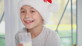 Cropped 4k video of little boy in Santa hat drinking milk and eating delicious cookies, licking milk mustache.
