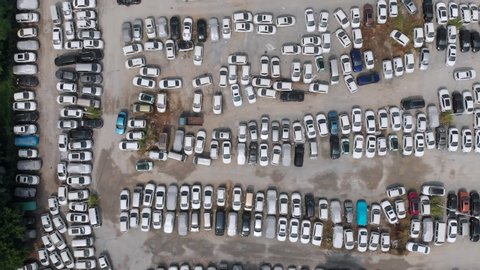We see a parking lot full of cars. Many cars of all colors and models are a little uneven. One white car maneuvering between the rest moves to the exit of the parking lot.