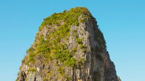 FullHD video - Huge limestone rock. with sparse vegetation clinging to its crumbling surface. towering over a tropical beach in timelapse.