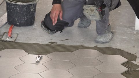 worker laying hexagon stone mass tiles on floor. Static closeup shot