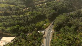Aerial footage from above view of green trees in Java Island countryside showing winding small road and small village
