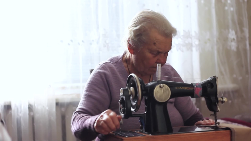 grandmother sew fabric clothes with a sewing machine