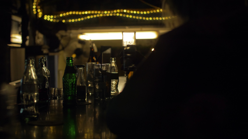 Silohuettes of people drinking in a bar at night. Glasses and bottles. Artificial lights and dark environment 