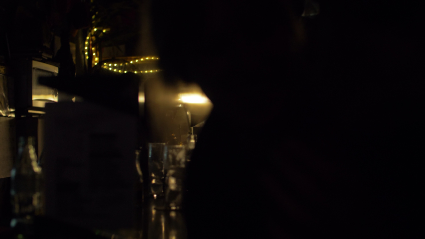 Silohuettes of people drinking in a bar at night. Glasses and bottles. Artificial lights and dark environment 