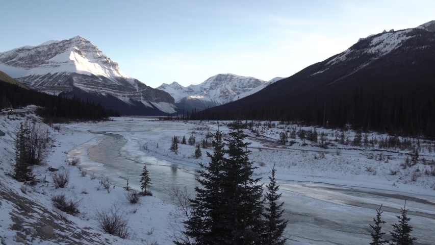 Panoramic view of the beautiful nature of the Jasper National Park in Canada with snowy forest, mountains and a icy river. Dolly shot.