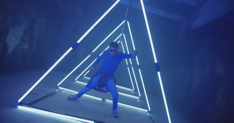 4K Professional Hip Hop break dancer . Stylish young man dancing with real strobe lights . Against colored background with triangle shape of led lights . Real decoration . Showing heart by fingers .