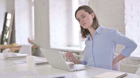 Tired Young Woman having Back Pain in Modern Office.