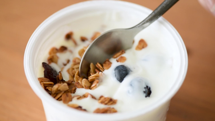Person eating yogurt with granola and blueberries from plastic jar. Greek yogurt breakfast or snack. Clean eating, vegetarian food concept | Shutterstock HD Video #1039863041