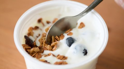 Person eating yogurt with granola and blueberries from plastic jar. Greek yogurt breakfast or snack. Clean eating, vegetarian food concept