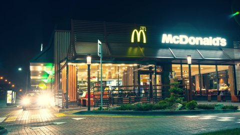 Belarus - Minsk, 27 October 2019. Timelapse shooting of Contemporary McDonald's exterior of night. Visitors to the restaurant come in and out at. cars drive up for their portion of fast food.