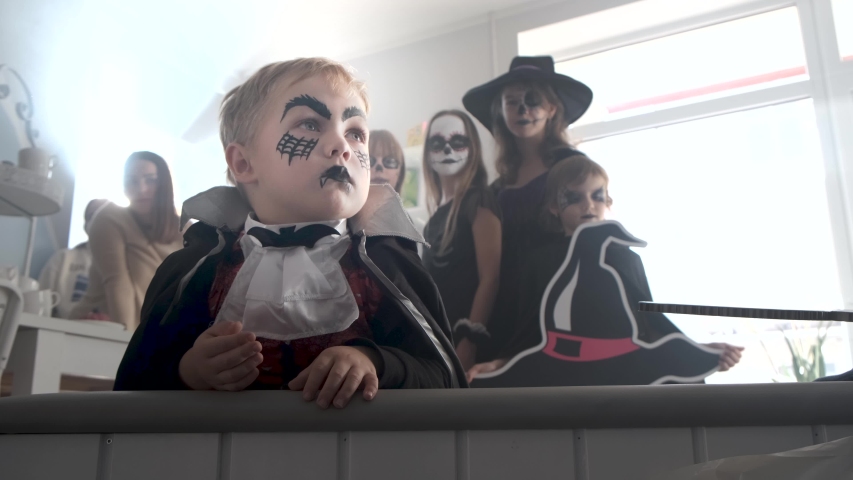 Kids in scary Halloween costumes have a great home party, they are performing with festive symbols, and coming clothier to the little Dracula boy.