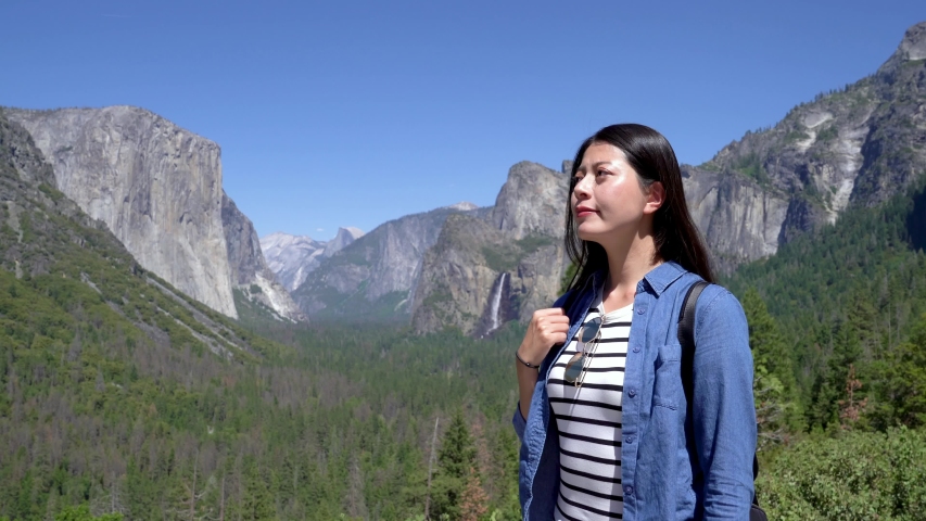 young beautiful asian woman hiker sightseeing tunnel view yosemite valley and bridalveil fall. happy female backpack standing outdoor hiking in mountains relax under sunshine looking around smiling