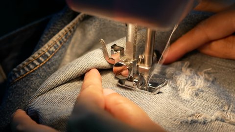 4K. close up of a woman sewing for repair blue denim jeans with a sewing machine