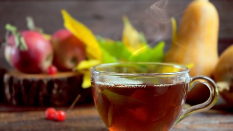 Hot tea on a wooden table against the background of the harvest (pumpkins, apples) and colorful autumn leaves. Stock Video
