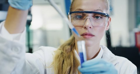 Portrait of blond female scientist is analyzing with a pipette a liquid to extract the DNA and molecules in the test tubes in laboratory. 