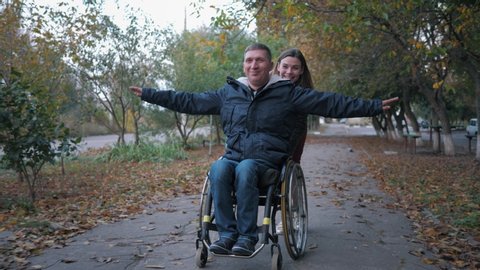 friendly support, happy disabled man have fun on a wheelchair ride and smiling female in autumn park Arkivvideo