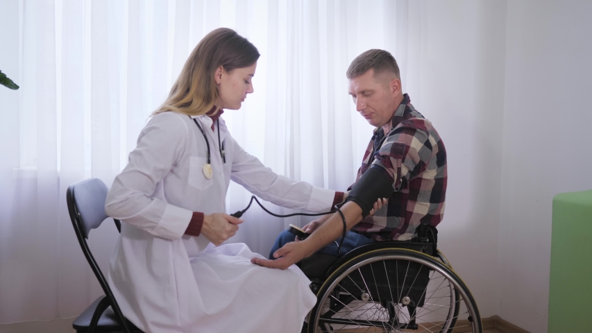 social worker during a physical examination measures pressure with a professional tool to a patient in a wheelchair