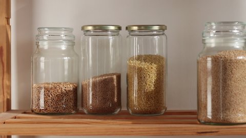 Zero Waste life, jars filled with brown rice, spelt, bulgur, couscous grain on a wooden shelf, warm light.