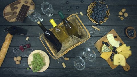 Red and white wine on exotic black table.
Red wine from black grapes and white wine from white grapes lie in basket in center of table. Nearby are: baguette, biscuits, blue cheese, grapes, cheese.