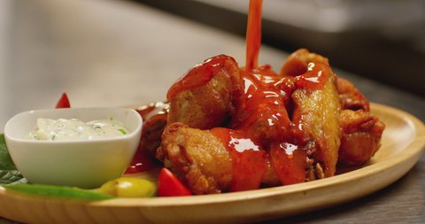 4K Bowl of buffalo wings with red and spicy sauce . Hot sauce pouring on chicken wings. Liquid pepper sauce pouring on chicken juicy meat into restaurant . Shot on RED Cinema camera in slow motion .  