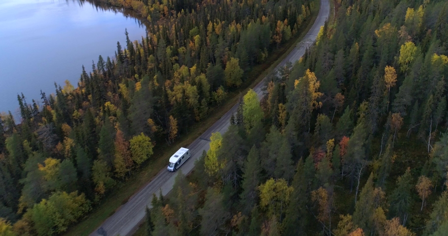Caravan on a forest road, Aerial, reverse, drone shot, following a camper rv, driving on a asphalt route, at lake Jerisjarvi, in middle of fall colored trees, on a cloudy, autumn day, in Pallas