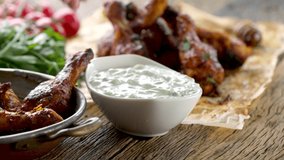BBQ chicken legs in woman hand and tzatziki dip sauce or dressing. Video shot 4K 50 fps.