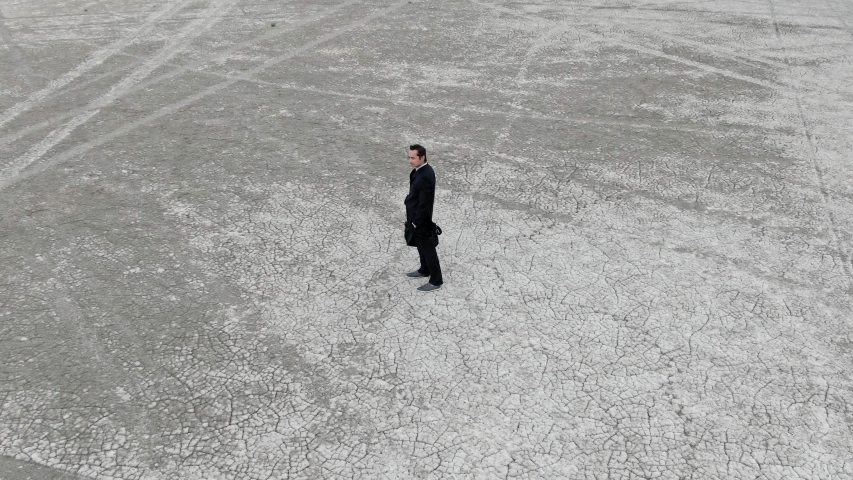 a man in a business suit with a briefcase in the desert throws out his briefcase and leaves