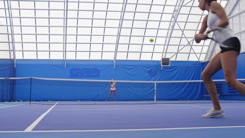 Panning shot of two sportswomen playing court tennis in sport hall with blue interior Stock Video