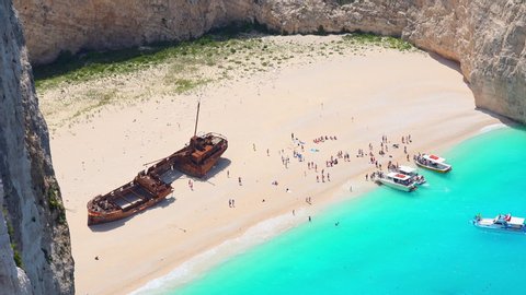 People relaxing and sunbathing on Navagio Beach or Shipwreck Beach. Old ship after crash lying on sand. Tourists swimming on turquoise Ionian Sea. Paradise in lagoon of Zakynthos island, Greece