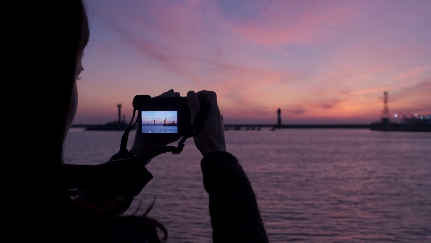 A woman on the beach at sunset takes a photo on the camera. Slow motion girl photographer at sunset photographing a beautiful and bright sunset.