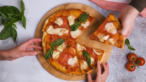 Top view of people hands taking slices of baking pizza
