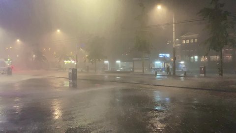 AMSTERDAM - CIRCA JUNE, 2019: Night footage of heavy rain and thunderstorms in Amsterdam. Tram passes and people walk.