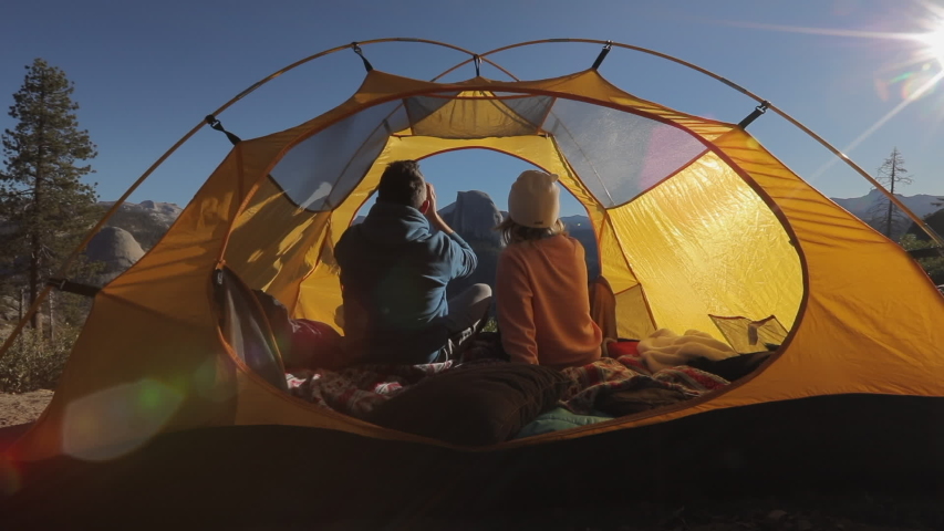Tourists sit in a tent at the backdrop of the tranquil picturesque landscape of Yosemite Valley and watch the Half Dome rock, that is seen straight forward, through the binoculars. Early morning.