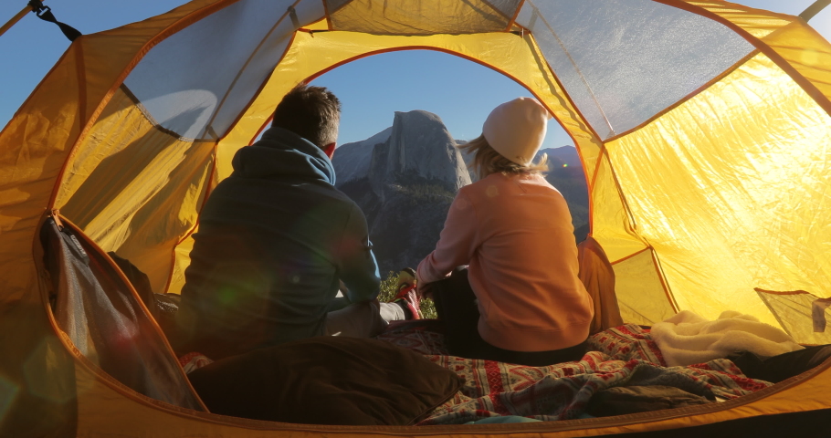 A pair of lovers hugging in a tent on the background of well-known rock formation, known as the Half Dome and located at the eastern part of Yosemite National Park. The dawn view. California. USA. 4K