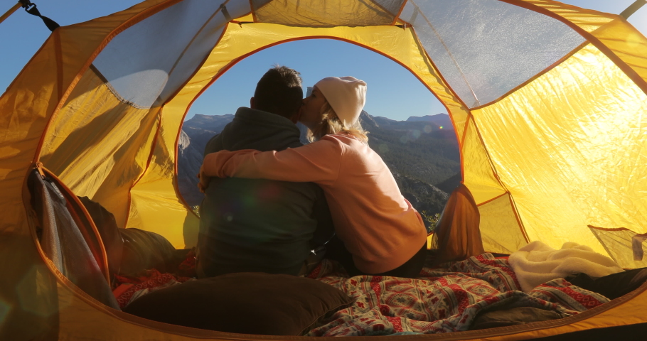 The romantic date of a couple in a beautiful Yosemite Valley. A man and a woman in a yellow touristic tent sit together and embrace against the background of Sierra Nevada mountains. 4K
