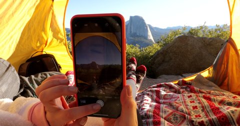 The girl takes a phone picture of the Half Dome cliff, which is very popular among tourists and is one of the symbols of Yosemite National Park. View of the mountain from inside the tourist tent. 2019