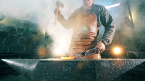 Working blacksmith shaping hot knife on anvil.