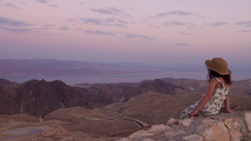 A little girl siting on the top of a mountain and looking at the mountains landscape