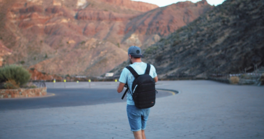 Bearded man photographer checking tuning his camera equipment outdoor. Handsome smiling hipster guy walking in beautiful mountains on perfect summer trip.