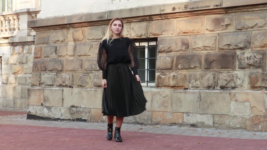 Stylish autumn fashionable video of a girl. Black wide-sleeved blouse, pleated skirt, blonde on old city background
