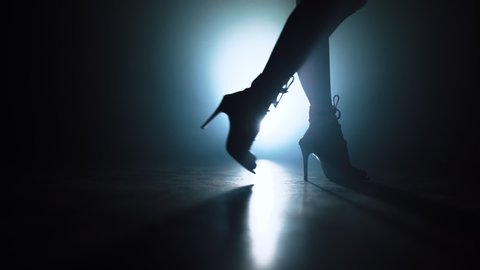 Woman in heels walks near camera across spotlight on smoky stage. Girl in sexy clothing. Nightclub dancer concept.