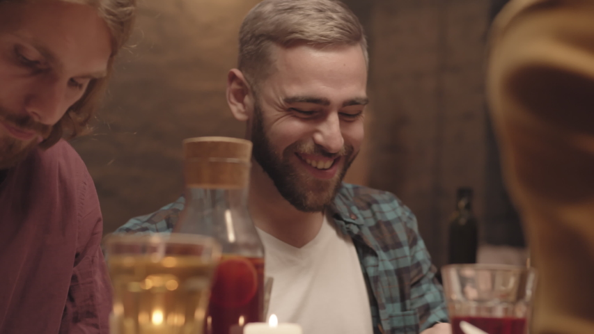 Handheld shot of happy man with beard eating and chatting with friends at dinner party | Shutterstock HD Video #1039960574