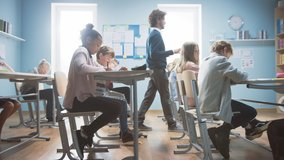 In Elementary School Class: Enthusiastic Teacher walks between Rows of Bright Diverse Children, Explains Lesson. Group of Smart Multiethnic Kids Learning New Stuff. Side View Tracking Shot - Powered by Shutterstock - Get 15% off with code: PIKWIZARD15