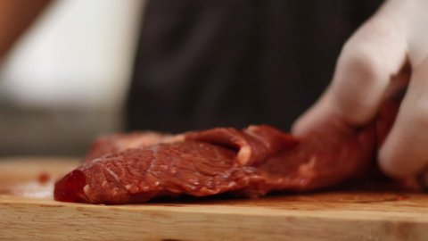 Close up hand and glove slicing red raw bee steak, on wooden slice board, daylight white glove, sharp small knife, black apron, chef prepare meat before cooking, steak, bbq, meat 4k