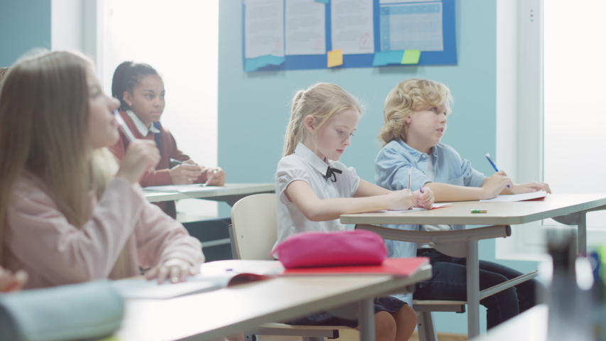 Elementary Classroom of Diverse Bright Children Listening Attentively to their Teacher Giving Lesson. Brilliant Young Kids Learning in School, Writing in Exercise Notebooks, Taking Tests.Moving Camera Royalty-Free Stock Footage #1039966946
