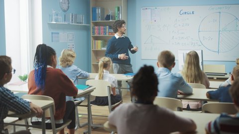 Caring Teacher Explains Lesson to a Classroom Full of Bright Diverse Children. In Elementary School with Group of Smart Multiethnic Kids Learning Science, Whole Classroom Raising Hands. Slow Motion